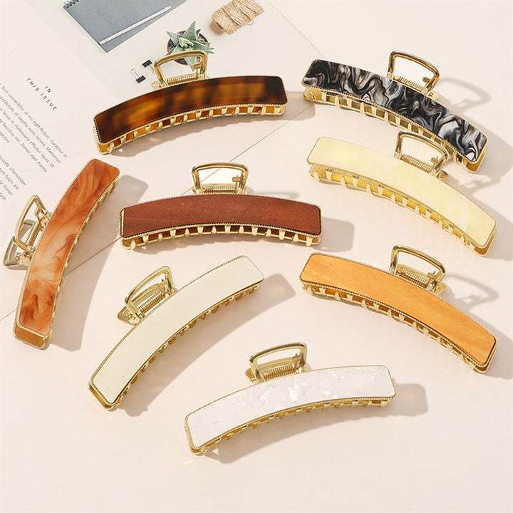 The SOHO Abby Hair Claw in Ginger by SOHO is a stylish rectangular clip, ideal for everyday wear, displayed with other colorful hair claws on a light surface next to a magazine and notepad.