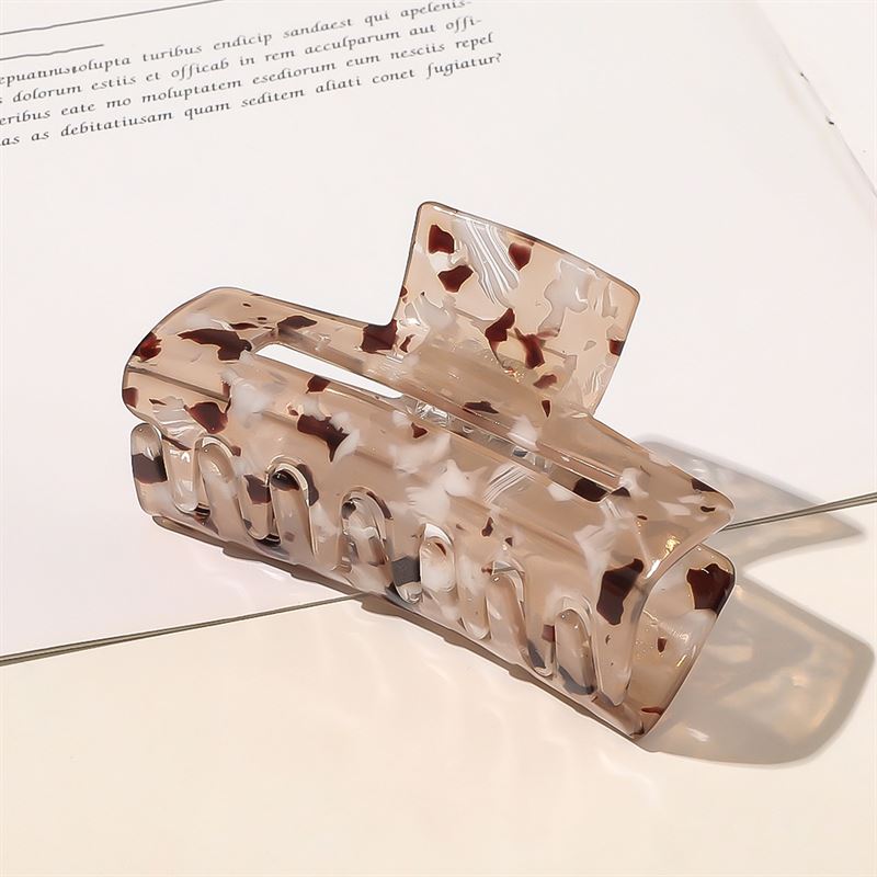 Die SOHO Aria Hair Claw in Light Tortoise liegt auf einem offenen Buch. Diese rechteckige SOHO-Klammer für dickes Haar verfügt über gebogene Zinken für einen sicheren Halt.