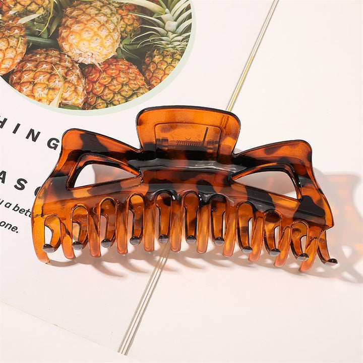 Die SOHO Astrid Hair Claw – Tortoise von SOHO, die für dickes Haar entwickelt wurde, liegt auf einer Magazinseite mit Ananasbildern und wirft einen deutlichen Schatten.