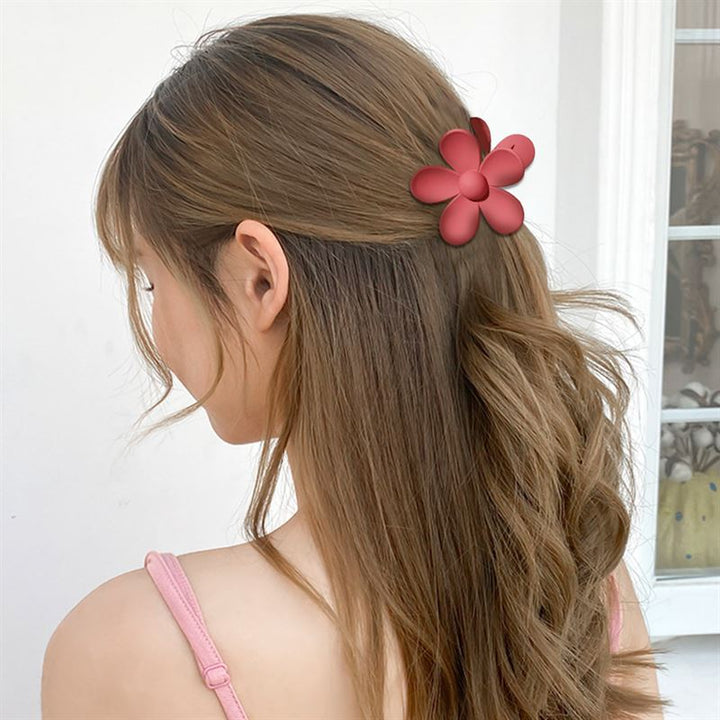 Eine Frau mit langen, welligen braunen Haaren trägt die SOHO Bloom Hair Claw in Gelb von SOHO, gestylt in Innenräumen, wobei sie der Kamera größtenteils den Rücken zuwendet.