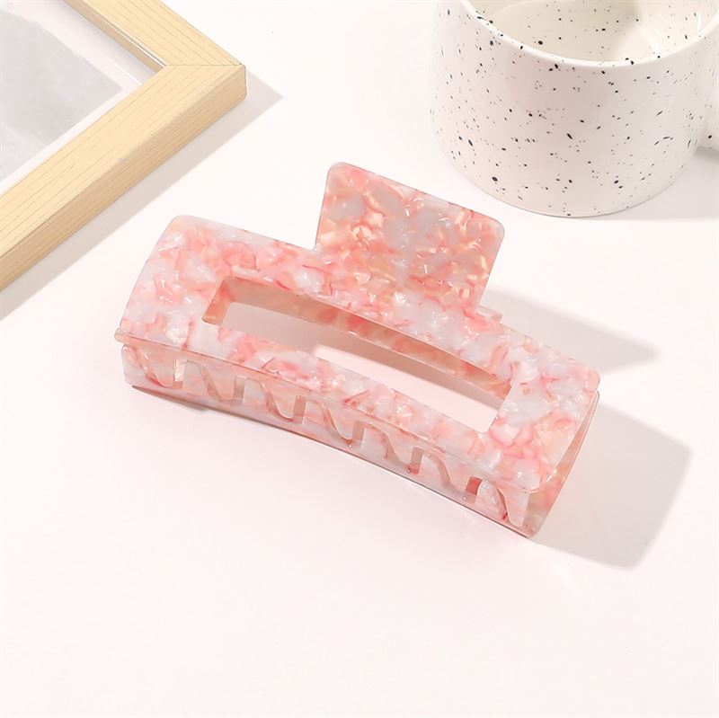 Die SOHO Clara Hair Claw in Light Coral (XL) liegt auf einer weißen Fläche neben einer gesprenkelten weißen Tasse und einem Bilderrahmen aus Holz.