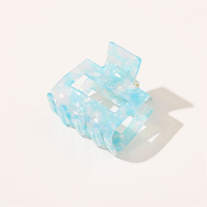 The SOHO Ema Hair Claw in Crystal Blue by SOHO features a translucent blue marbled design, shown on a white background with a soft shadow—a chic accessory ideal for elegant hairstyles.