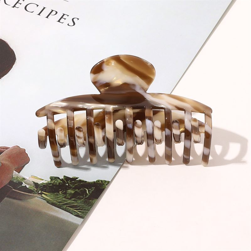 The SOHO Gaja Hair Claw in Brown Marble by SOHO sits atop an open magazine, casting a stylish shadow—a chic marbled accessory perfect for elevating your everyday look.