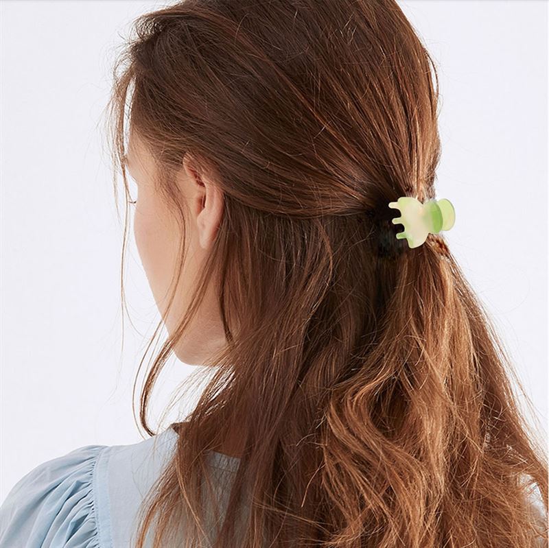 Eine Frau mit langen, welligen braunen Haaren ist von hinten zu sehen, ihr Haar ist teilweise mit der SOHO Hara Mini Hair Claw in Periwinkle zurückgebunden. Sie trägt eine hellblaue Bluse für einen weichen, eleganten Look.