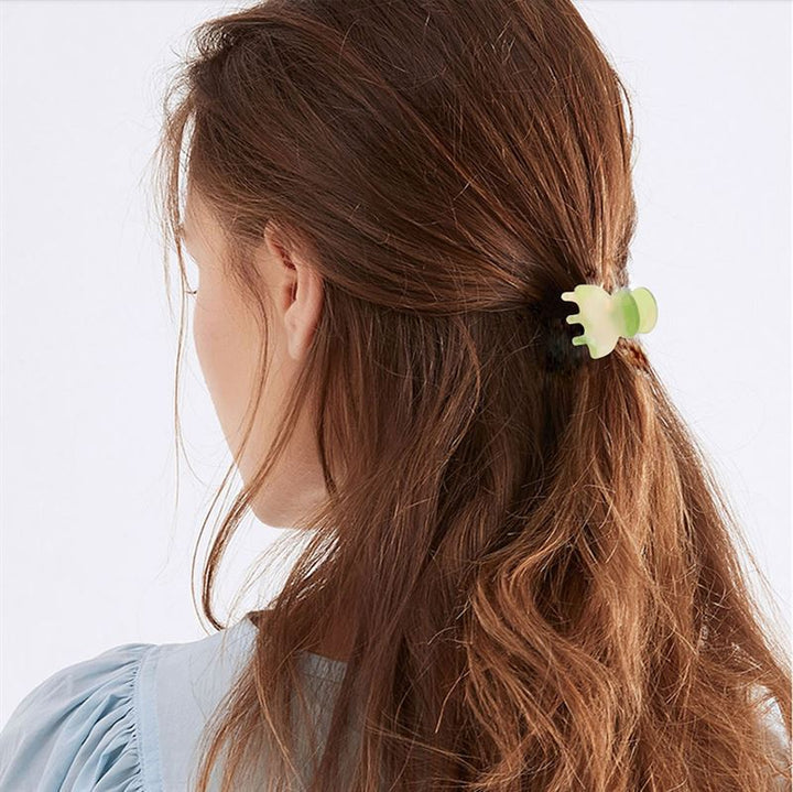 Eine Frau mit langen, welligen braunen Haaren ist von hinten zu sehen, ihr Haar ist teilweise mit der SOHO Hara Mini Hair Claw in Periwinkle zurückgebunden. Sie trägt eine hellblaue Bluse für einen weichen, eleganten Look.