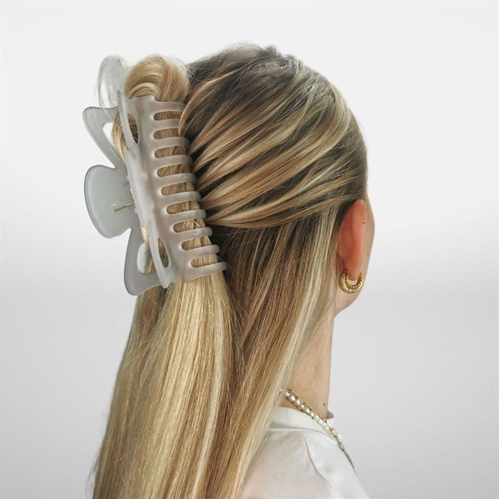 A woman with long blonde hair in a half-up twist, secured by the SOHO Jelly Hair Claw in Cloudy Grey, suitable for all hair types. She wears gold hoop earrings and a pearl necklace, viewed from behind.
