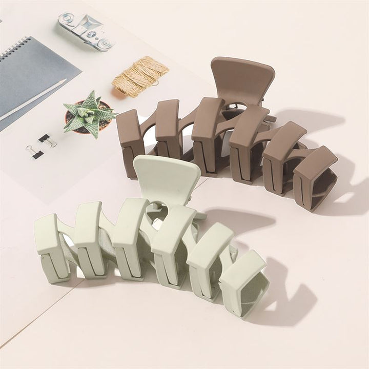 The SOHO Just Hair Claw in brown by SOHO rests elegantly on an open magazine with stationery and a geometric paper star, softly lit to highlight its matte finish and stylish design against a pale background.