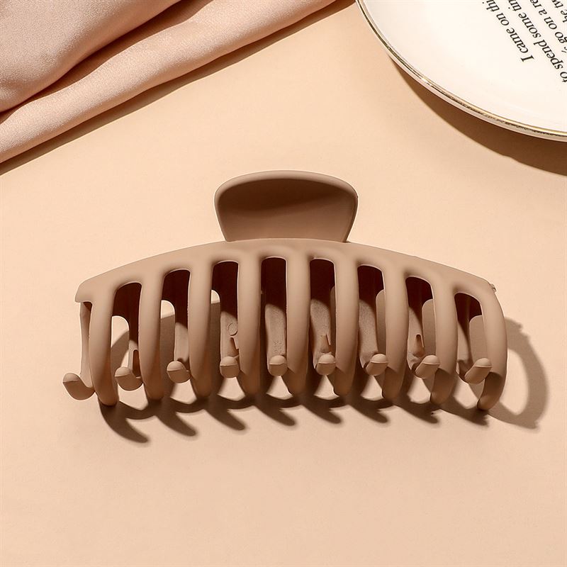 The SOHO Kana Hair Claw in beige features wide, curved prongs for a strong grip on all hair types, and is shown on a light tan surface near a white plate and beige fabric.