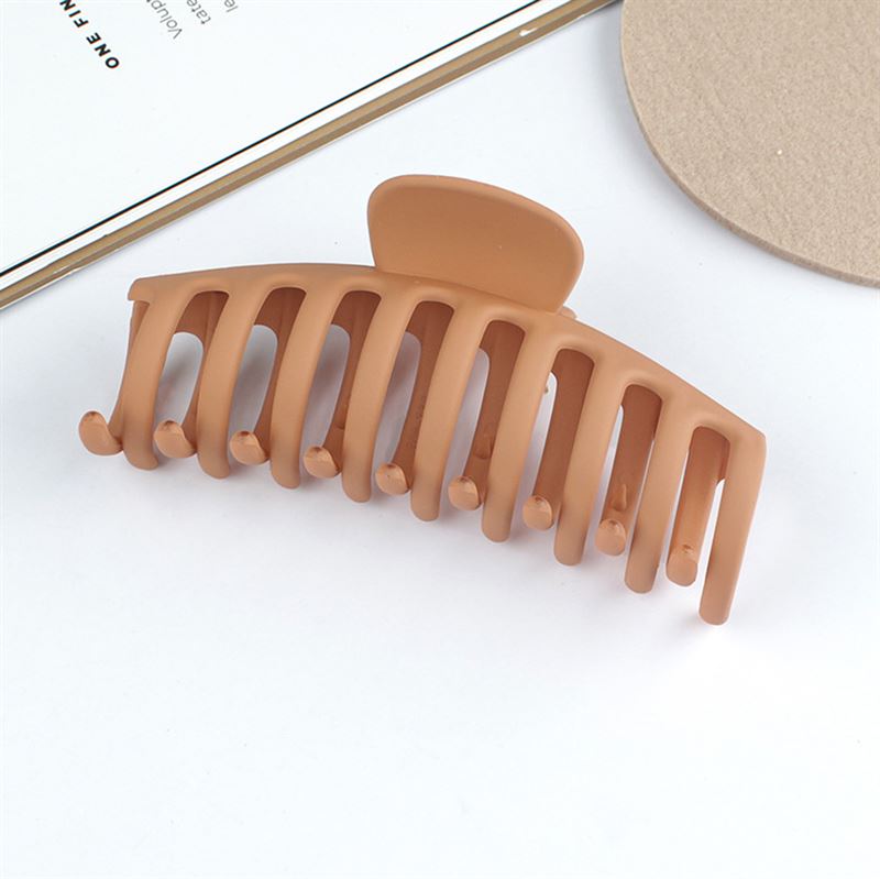The SOHO Kana Hair Claw - Sepia by SOHO, a brown matte wide-tooth clip for all hair types, is shown on a white surface beside a round beige item and a partially visible book or notebook.