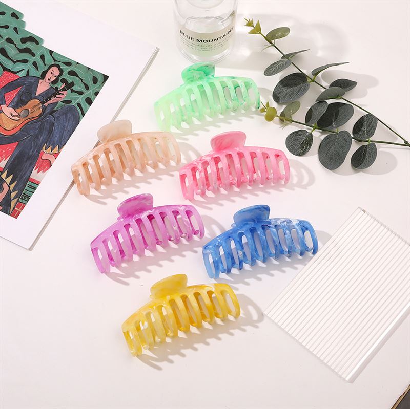The SOHO Kana Marble Hair Claw - Ocean by SOHO is displayed on a white surface beside a leafy branch, a clear bottle, lined sheet, and guitar artwork—an ideal hair accessory to add style to your everyday look.