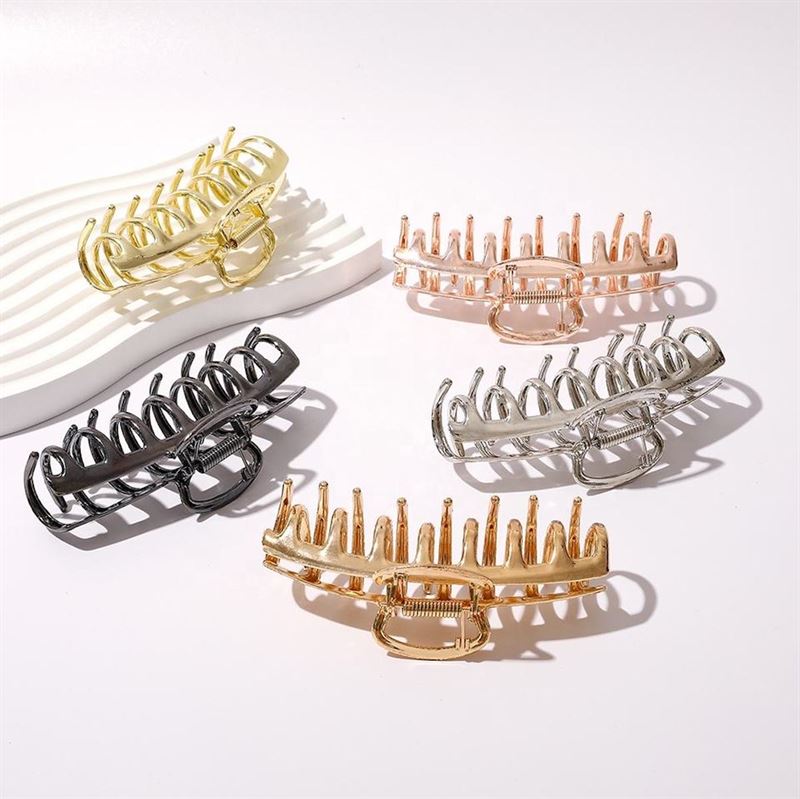Fünf große SOHO Kana Metal Hair Claw-Clips in Gold, Roségold, Silber, Bronze und Schwarz sind auf einer weißen Fläche angeordnet. Auf einem weißen Tablett im Hintergrund liegt der SOHO Kana Metal Hair Claw – Gold.