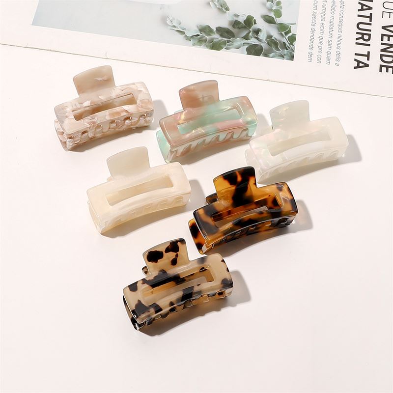 Die SOHO Leia Mini Hair Claws in Schildpatt- und neutralen Marmormustern werden auf einer weißen Oberfläche präsentiert, ideal für das Haarstyling. In der Ecke ist ein Magazin zu sehen.