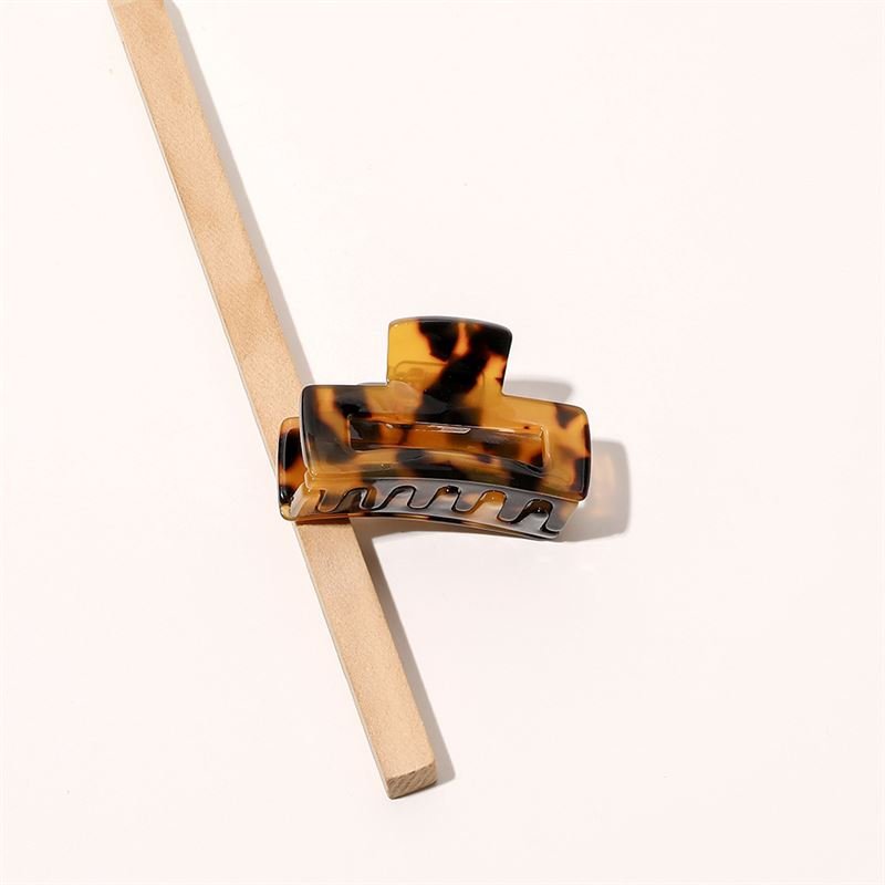 Die SOHO Leia Mini Hair Claw – Tortoise von SOHO ruht auf einem diagonal platzierten Holzstab vor einem hellen Hintergrund und eignet sich perfekt für müheloses Haarstyling.