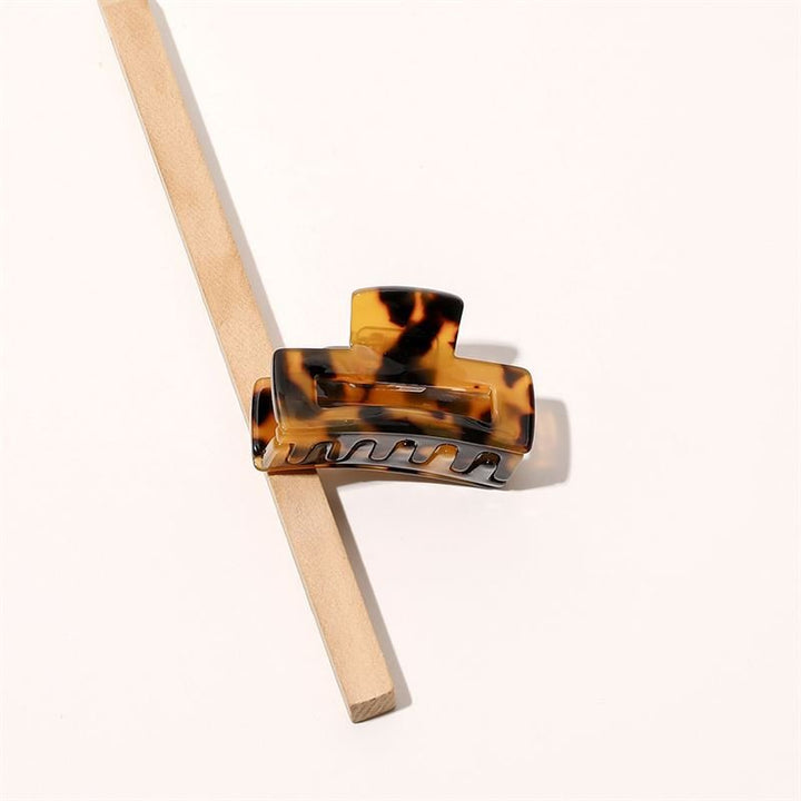 Die SOHO Leia Mini Hair Claw – Tortoise von SOHO ruht auf einem diagonal platzierten Holzstab vor einem hellen Hintergrund und eignet sich perfekt für müheloses Haarstyling.