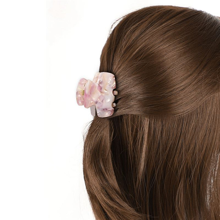 Nahaufnahme von braunem Haar, das hinten mit der SOHO Loa Mini Hair Claw in White Marble mit rosa-weißem Marmormuster befestigt ist. Der Hintergrund ist einfarbig weiß.