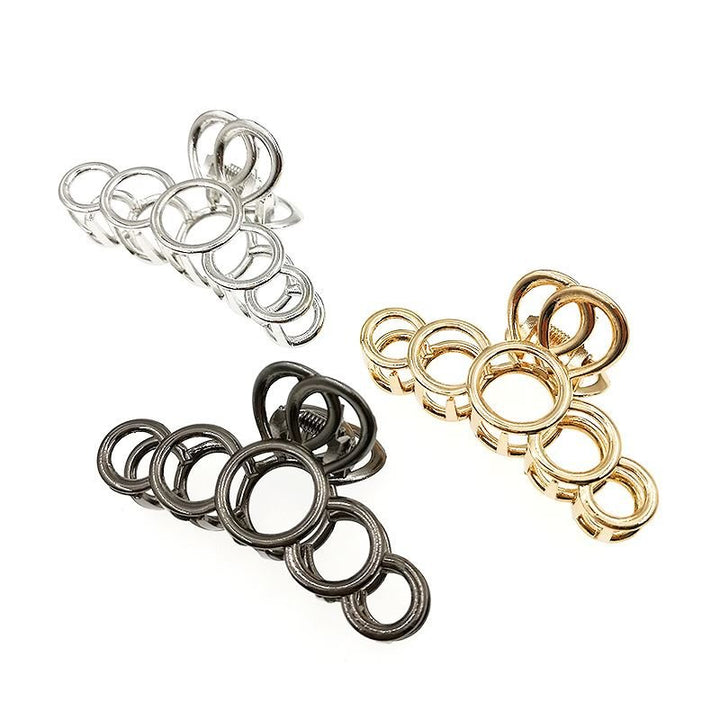 Die SOHO Metal Hair Claw in Silber von SOHO besteht aus ineinandergreifenden Metallringen unterschiedlicher Größe, die dickes Haar stilvoll und elegant fixieren, und wird auf weißem Hintergrund präsentiert.