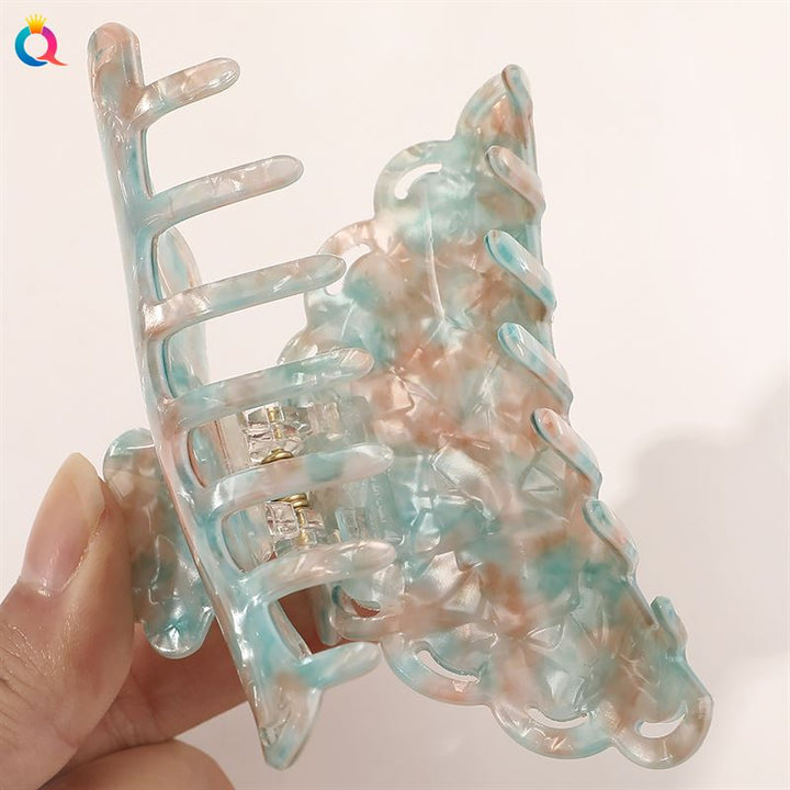 Eine Hand hält die SOHO Naomi Hair Claw – Sunshine von SOHO – ein großes, marmoriertes Accessoire in Pastelltönen, das jede Frisur aufwertet – vor einem einfarbigen hellen Hintergrund.