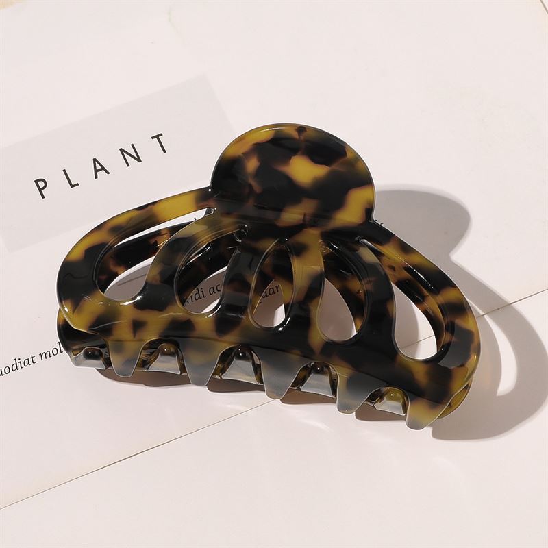 Die SOHO Olivia Hair Claw in Dark Tortoise mit breiten, gebogenen Zinken liegt auf einer weißen Oberfläche, unter der teilweise „PLANT” zu sehen ist – perfekt, um Ihrem Stil einen schicken Touch zu verleihen.
