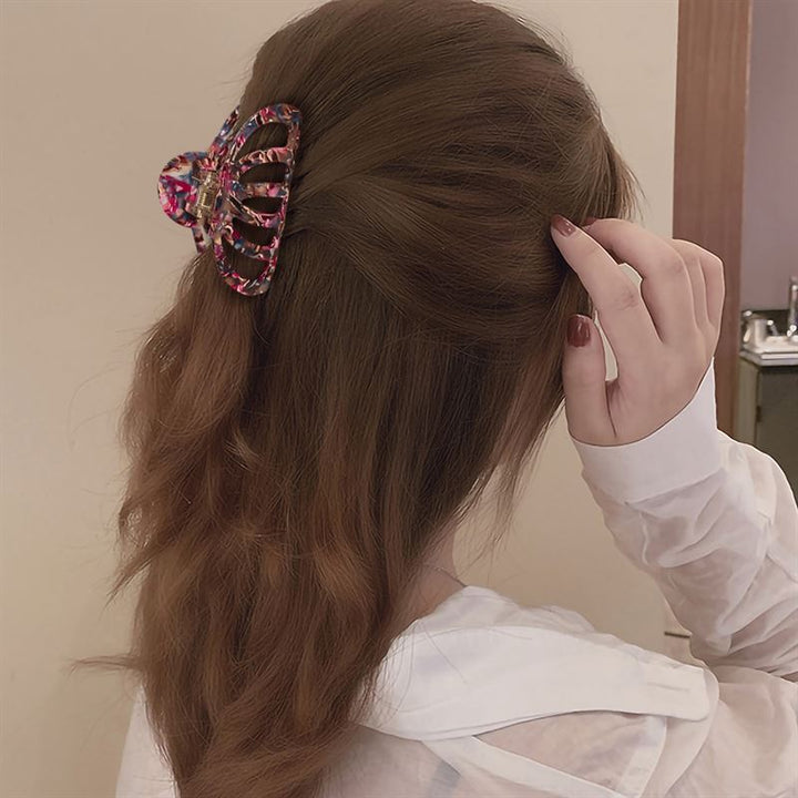 Mit welligem braunem Haar, das mit der SOHO Olivia Hair Claw – Dark Tortoise halb hochgesteckt ist, berührt eine Person in einem weißen Hemd mit einer Hand ihr Haar, während sie der Kamera den Rücken zuwendet.