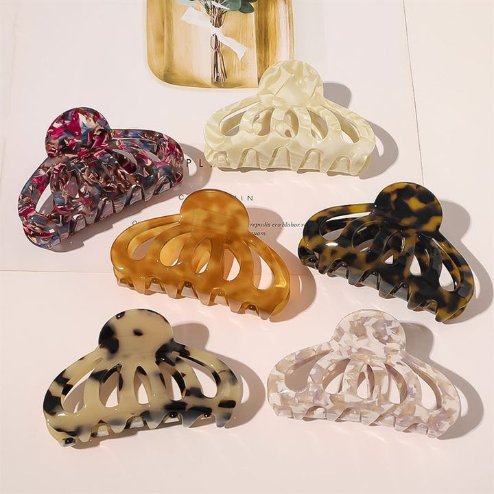 Sechs SOHO-Haarspangen mit Muster, darunter die SOHO Olivia Hair Claw – Dark Tortoise, sind in einem Halbkreis auf einem Magazin angeordnet und zeigen Designs in Marmorrosa, Creme, Bernstein, Schildpatt, Schwarz-Weiß und schillerndem Weiß.