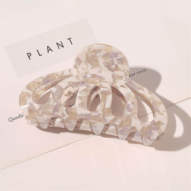 Die SOHO Olivia Hair Claw – Marble, ein Accessoire von SOHO mit pastellfarbenem Marmormuster, liegt auf einer weißen Oberfläche mit aufgedrucktem Text und sanften Schatten und verleiht jedem Stil einen schicken Touch.