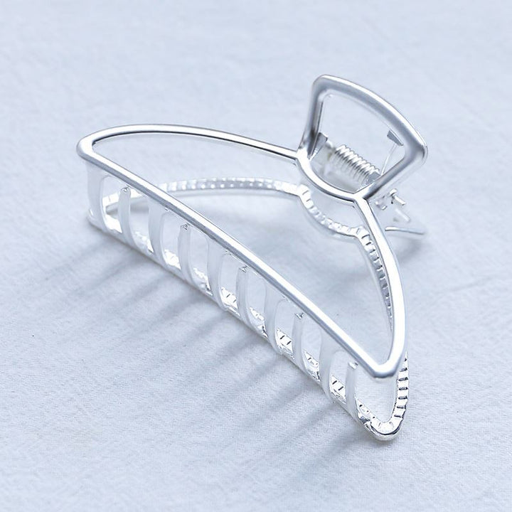 The SOHO Tori Small Metal Hair Claw in matt silver features a geometric open-frame design, perfect for securing messy buns—an elegant and essential hairstyle accessory by SOHO, shown on a light textured surface.