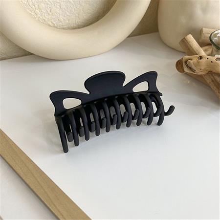 Die SOHO Zara Hair Claw – Black von SOHO mit mattem Finish und gebogenen Zinken liegt auf einer weißen Oberfläche mit beigem Dekor und Holzakzenten im Hintergrund.