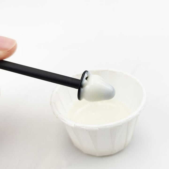 A hand holds a black tool with a dental mold tip, covered in white wax, above a cup from the UNIQ Nose Wax Kit by UNIQ for easy nose hair removal.
